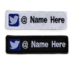 May include: Two rectangular patches, one white and one black, with embroidered text. Each patch features a blue bird logo in a square, the @ symbol, and the words "Name Here".