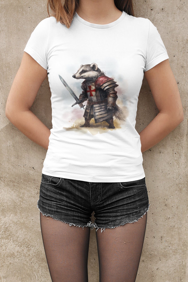 Pode incluir: Camiseta branca com uma ilustra&ccedil;&atilde;o em aquarela de um texugo com armadura de cavaleiro, segurando uma espada. O texugo usa um capacete e uma cruz vermelha no peito. A camiseta &eacute; combinada com shorts jeans pretos.