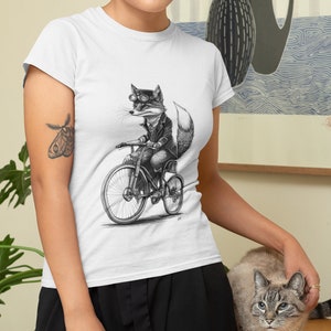 以下が含まれることがあります： 自転車に乗ったゴーグルをかけたキツネの白黒イラストが描かれた白いTシャツ