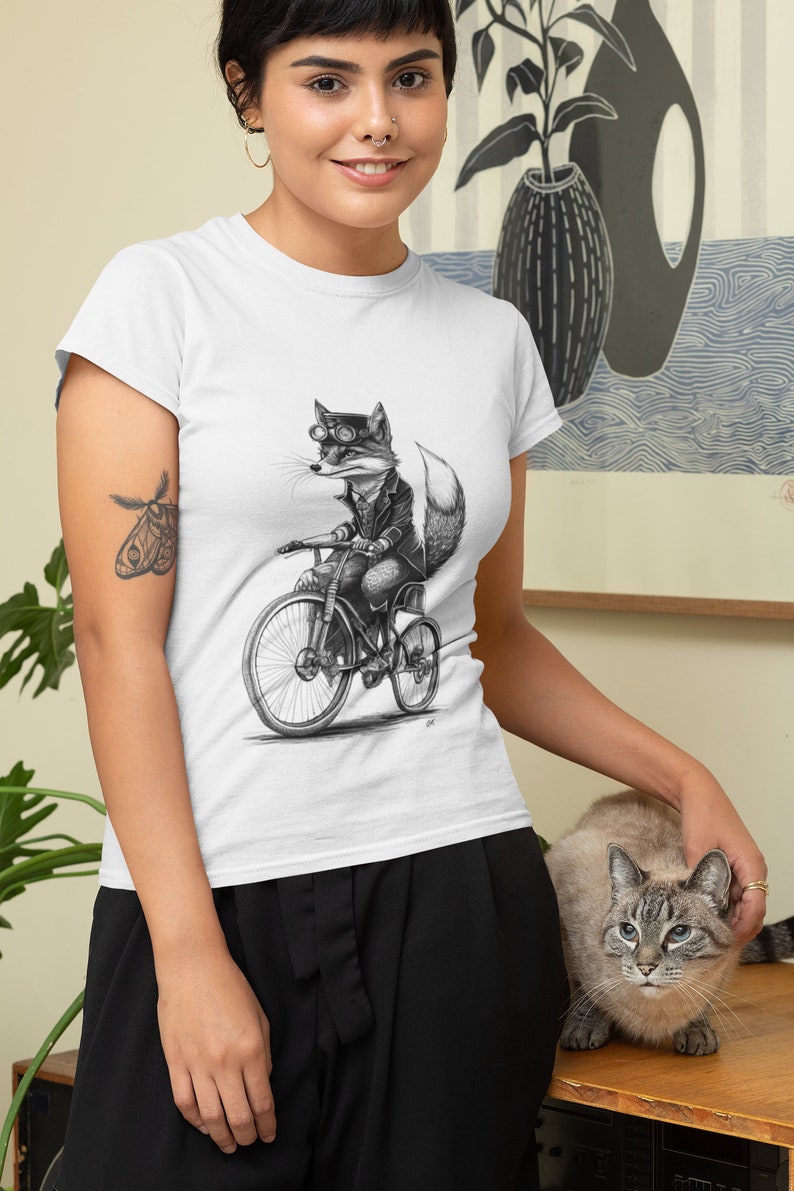 以下が含まれることがあります： 自転車に乗ったゴーグルをかけたキツネの白黒イラストが描かれた白いTシャツ