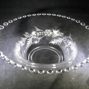 May include: A clear glass bowl with a beaded rim and an etched design of grapes and leaves.