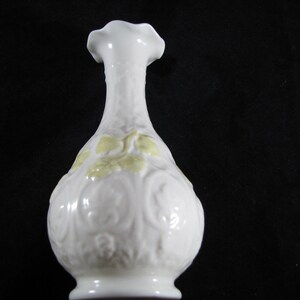 May include: A white ceramic vase with a yellow floral design. The vase has a round body and a narrow neck.