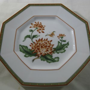May include: White octagonal porcelain plate with a green and gold border. The center features a floral design with orange and yellow chrysanthemums, green leaves, and a small orange butterfly.