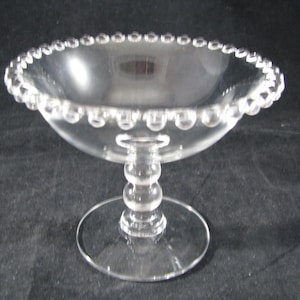May include: A clear glass pedestal bowl with a beaded rim and a round base.