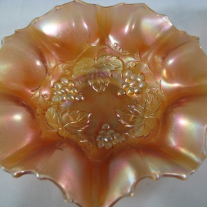 May include: A vintage iridescent glass bowl with a ruffled edge and a grapevine design. The bowl is a pale orange color with a pearlescent finish.