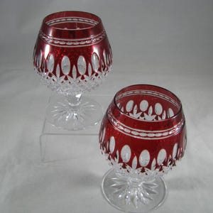 May include: Two clear glass stemmed goblets with a red base and intricate cut glass designs.