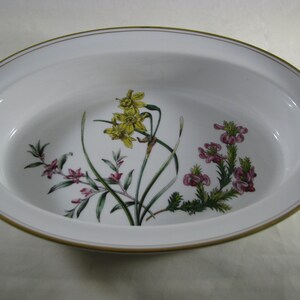 May include: White oval serving dish with a gold rim. The dish features a floral design with yellow daffodils and pink flowers.