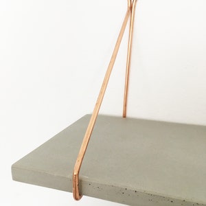 May include: A gray concrete shelf with copper metal brackets. The shelf is mounted to a white wall.