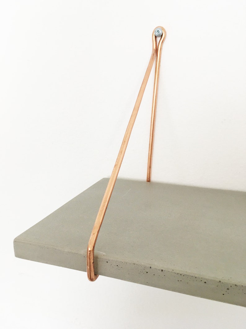 May include: A gray concrete shelf with copper metal brackets. The shelf is mounted to a white wall.