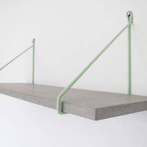 May include: A concrete shelf with light green metal brackets. The shelf is mounted to a white wall.