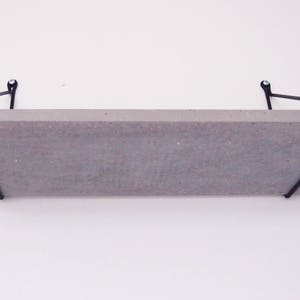 May include: A concrete shelf with black metal brackets. The shelf is mounted to a white wall.