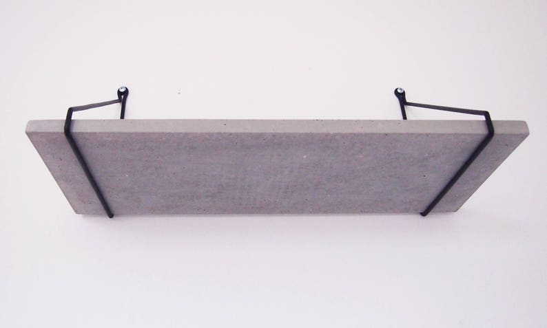 May include: A concrete shelf with black metal brackets. The shelf is mounted to a white wall.