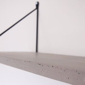 May include: A concrete shelf with a black metal bracket. The shelf is light gray and has a rough texture.