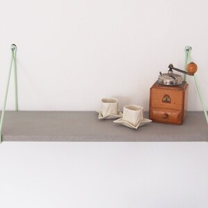 May include: A gray wooden shelf with two white ceramic cups and a vintage coffee grinder on top. The shelf is suspended from the ceiling with two light green cords.