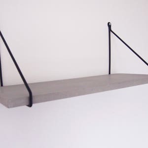 May include: A gray floating shelf with black metal triangular brackets. The shelf is mounted to a white wall.