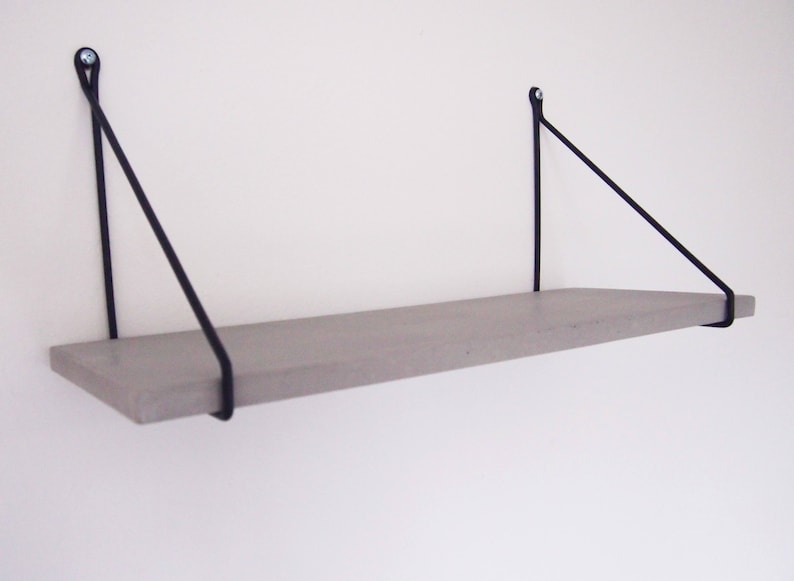 May include: A gray floating shelf with black metal triangular brackets. The shelf is mounted to a white wall.
