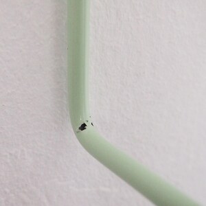 May include: Close-up of a light green metal hook with a small chip in the paint.