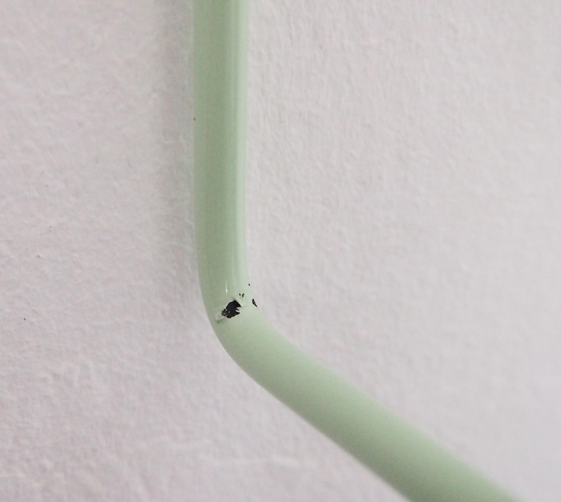 May include: Close-up of a light green metal hook with a small chip in the paint.