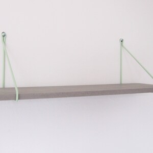 May include: A gray wooden shelf with light green rope supports attached to the wall.