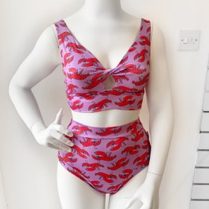 Op de afbeelding: Een paarse badpak met een kreeftprint. De top heeft een geknoopt detail aan de voorkant en de broek is hoog getailleerd.