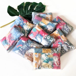May include: A collection of colourful, clear plastic bags containing various printed fabric squares. Each bag features the text "I'm 100% eco friendly" and a different design.