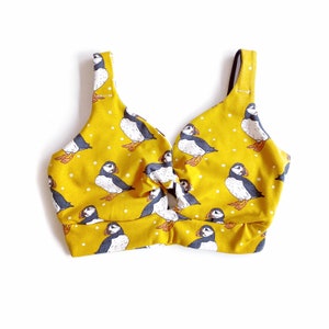 May include: Yellow crop top with a knotted front and a print of black and white puffins.