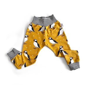 May include: Yellow baby leggings with a black and white striped waistband and a pattern of puffins.