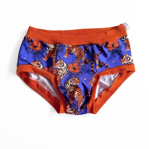Op de afbeelding: Blauw ondergoed met een oranje rand en een tijgerprint. Het ondergoed heeft een herhalend patroon van oranje tijgers en oranje bloemen op een blauwe achtergrond. De rand is effen oranje.