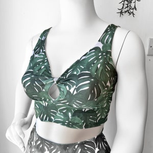 Op de afbeelding: Een groen en wit crop top met een tropische bladerenprint. De top heeft een sleutelgat-uitsparing aan de voorkant en een geknoopt detail.