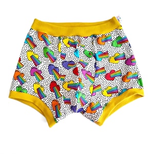 May include: Boxer shorts with a white background covered in black polka dots and colorful heart and rainbow graphics. The waistband and trim are bright yellow. The shorts are made of a soft, comfortable material.