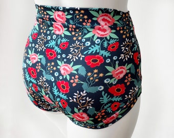 Pode incluir: Calção de banho preto de cintura alta com estampa floral com flores vermelhas, rosas e verdes sobre um fundo azul escuro.