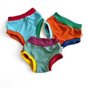 May include: Three pairs of colourful cotton underwear with contrasting coloured trim. The underwear is in shades of teal, orange, red, yellow, green, and purple.