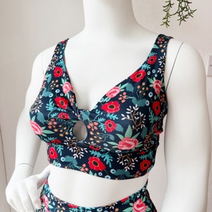 May include: A black and green floral print crop top with a keyhole cutout in the front. The top has a V-neckline and thin straps.