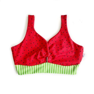 Peut inclure: Un haut de maillot de bain rouge et vert à imprimé pastèque. Le haut a un devant noué et une bande rayée verte et blanche.