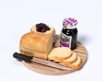 May include: A wooden cutting board with a loaf of bread, a jar of blackberry jam, and a butter knife. The bread is sliced and ready to be spread with jam.