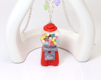 May include: A red gumball machine pendant necklace with a clear glass globe filled with colorful gumballs. The necklace has a silver chain and a silver clasp.
