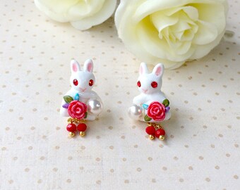 May include: White bunny rabbit earrings with red roses and pearl accents. The earrings have a dangling red bead charm.