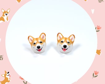 May include: A pair of brown and white corgi dog earrings. The corgis are smiling with their tongues sticking out.