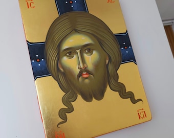 May include: A hand-painted icon of Jesus Christ with a gold background and a blue cross. The icon is framed in a wooden frame with a red border. The text "IC XC NI KA" is written in red on the frame.