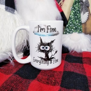 May include: White ceramic coffee mug with a black and white illustration of a cat with large eyes and the text "I'm Fine Everything is Fine".