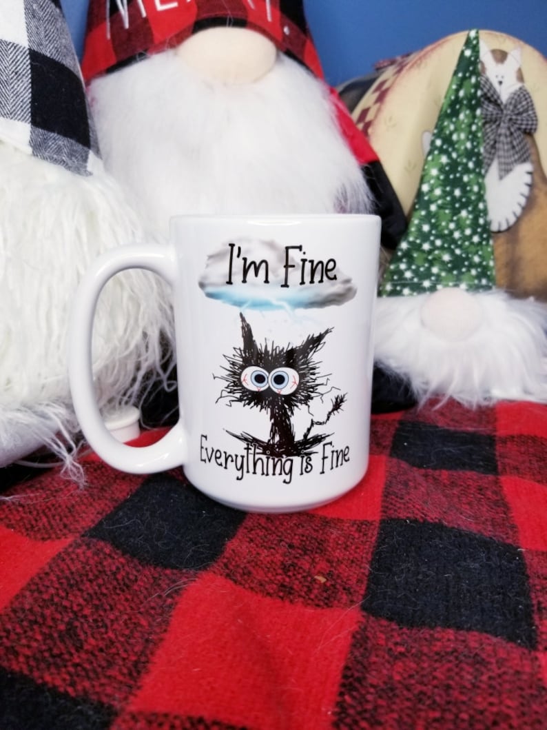 May include: White ceramic coffee mug with a black and white illustration of a cat with large eyes and the text "I'm Fine Everything is Fine".