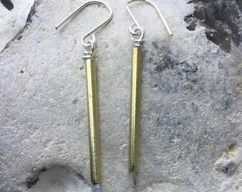 May include: A pair of gold and silver earrings with a long, thin, gold bar pendant. The earrings are hanging from a silver hook.