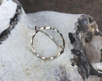 May include: A silver ring with a hammered, circular design. The ring is simple and minimalist, with a smooth, polished finish.