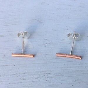May include: A pair of silver stud earrings with a rose gold bar accent. The bar is slightly curved.