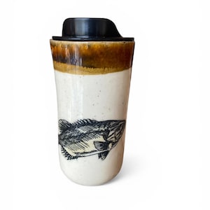 May include: A ceramic travel mug with a black lid and a fish illustration. The mug has a speckled white body with a brown band near the top. The fish is a detailed black and white drawing.