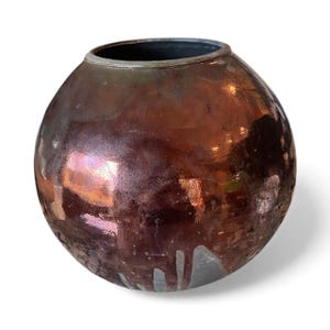 May include: A round, glazed ceramic vase with a dark brown exterior and a black interior. The vase has a metallic sheen with hints of purple and orange. The bottom of the vase has a drip effect.