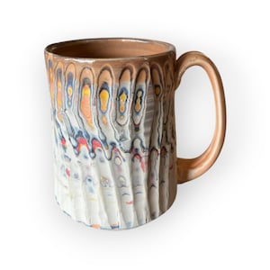 Pode incluir: Caneca de cerâmica artesanal com um design texturizado único. A caneca apresenta uma alça e borda marrom claro, com um corpo branco e multicolorido. As cores incluem laranja, amarelo, azul e vermelho. Capacidade de aproximadamente 350 ml.