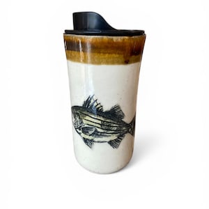 May include: White ceramic travel mug with a black lid and a brown band near the top. The mug features a detailed black and white illustration of a fish. The mug is designed for hot or cold beverages.