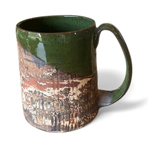 Puede incluir: Una taza de cerámica hecha a mano con un diseño único. La mitad superior es de color verde brillante, mientras que la mitad inferior presenta un patrón texturizado con tonos marrones, rojos y blancos. La taza tiene un asa curvada.