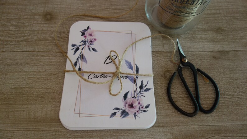 May include: A stack of white cards with a floral design and gold accents. The cards are tied together with twine and the text "12 Cartes - Pages" is visible.